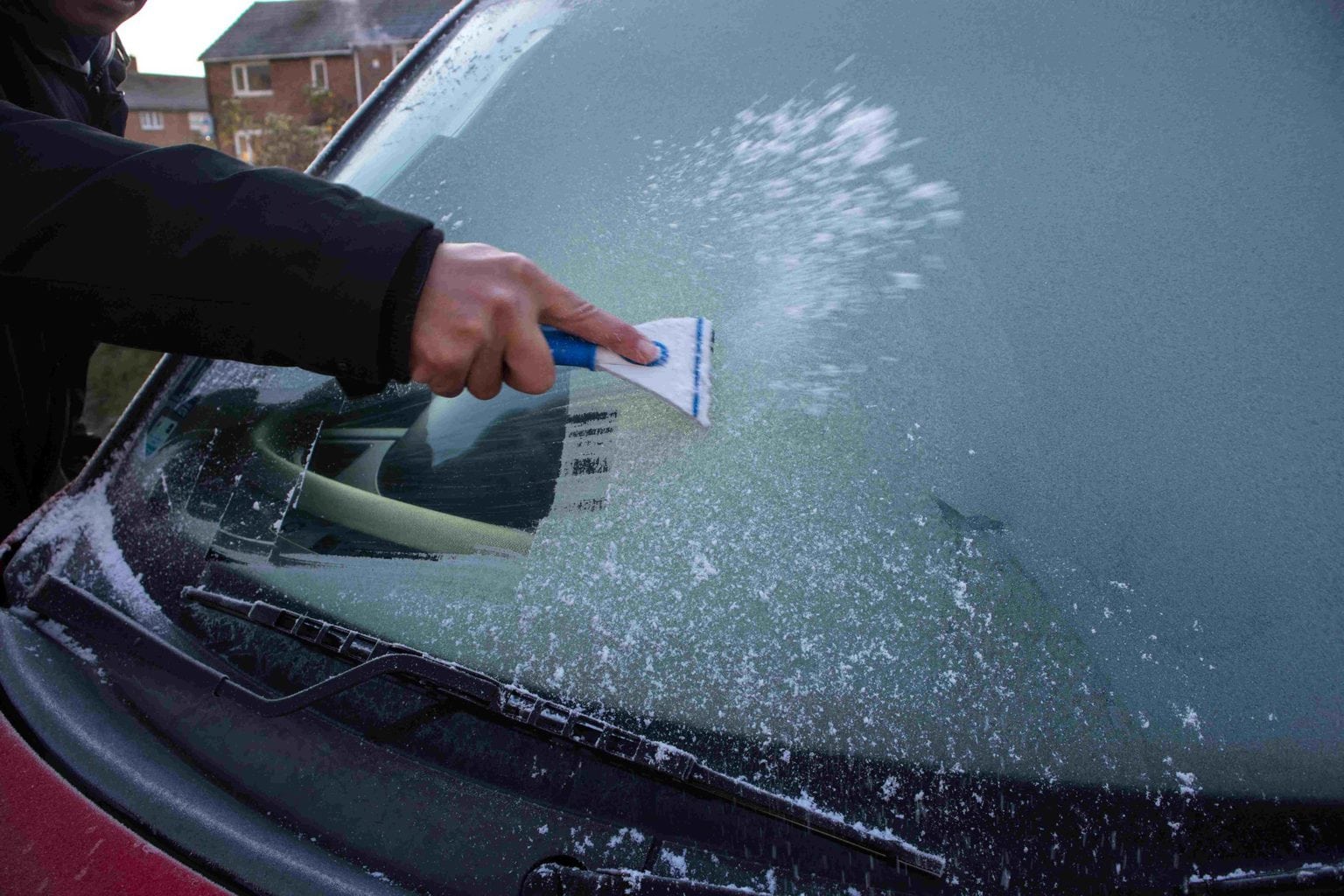 De-icing the windscreen of a car. This is an important winter driving safety tip for employees.